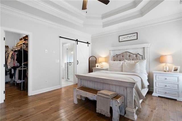 bedroom with crown molding, a walk in closet, a barn door, hardwood / wood-style flooring, and a raised ceiling