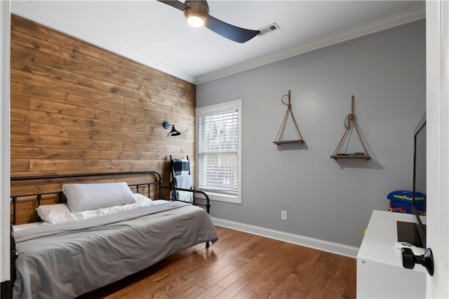 bedroom with visible vents, crown molding, baseboards, wood finished floors, and a ceiling fan