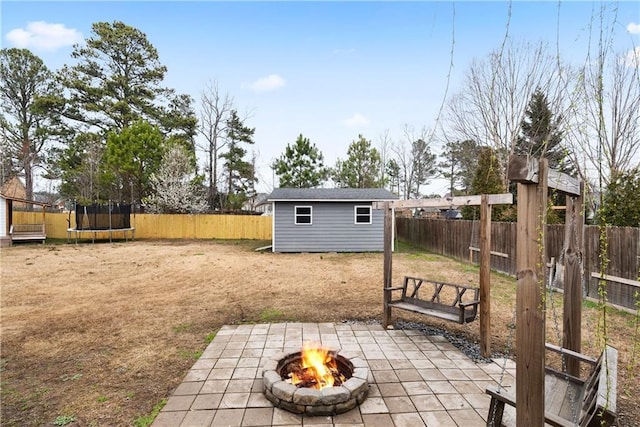 view of yard featuring a patio, an outdoor fire pit, a fenced backyard, an outdoor structure, and a trampoline