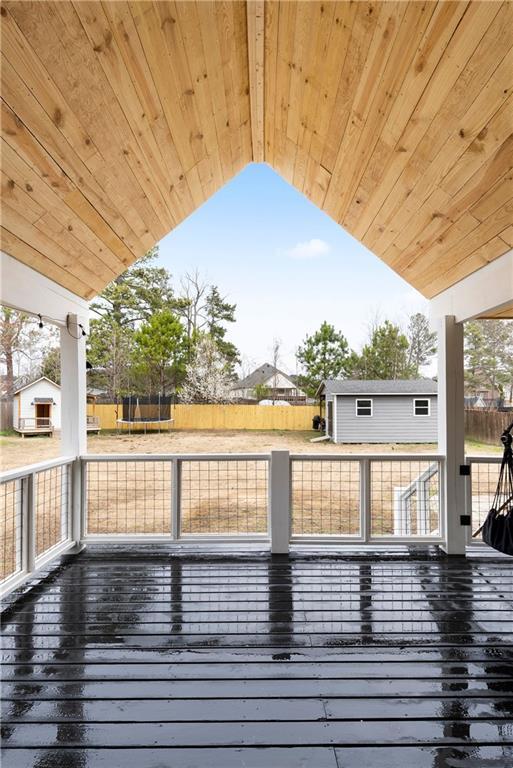 wooden deck with an outdoor structure, a trampoline, and fence