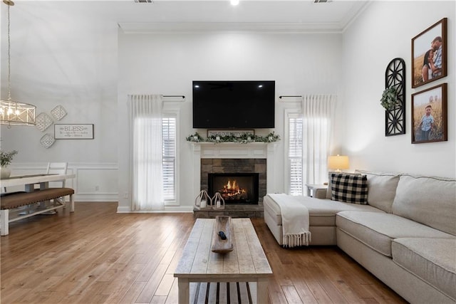 living room featuring a high ceiling, ornamental molding, a stone fireplace, wood-type flooring, and a chandelier