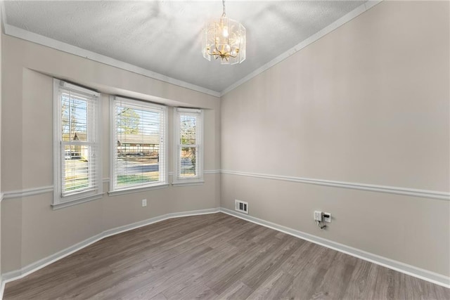 empty room featuring lofted ceiling, a textured ceiling, ornamental molding, a notable chandelier, and hardwood / wood-style floors