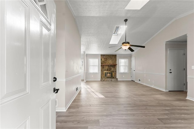 unfurnished living room with a stone fireplace, vaulted ceiling with skylight, ceiling fan, and light hardwood / wood-style flooring