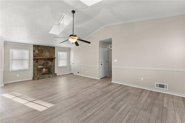 unfurnished living room with light hardwood / wood-style flooring, a fireplace, lofted ceiling with skylight, and ceiling fan