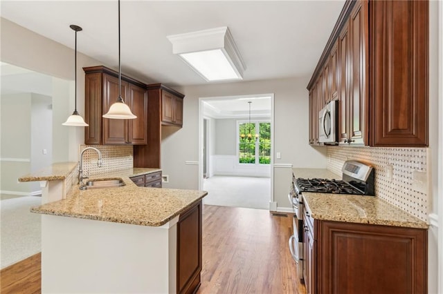 kitchen featuring a peninsula, light stone countertops, light wood-style floors, a sink, and stainless steel appliances