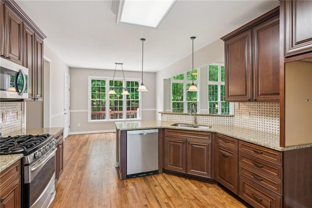 kitchen with a sink, light wood-style flooring, appliances with stainless steel finishes, and backsplash