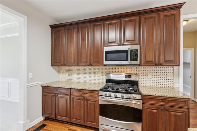 kitchen with visible vents, light wood-type flooring, tasteful backsplash, light stone counters, and stainless steel appliances