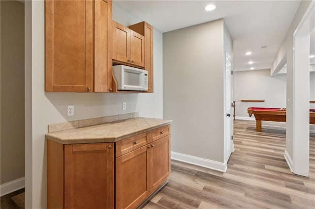 kitchen featuring tile countertops, baseboards, light wood-type flooring, and white microwave