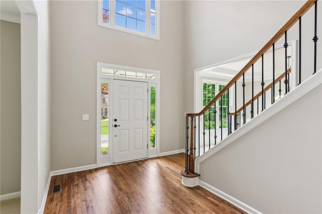foyer featuring visible vents, wood finished floors, baseboards, a high ceiling, and stairway