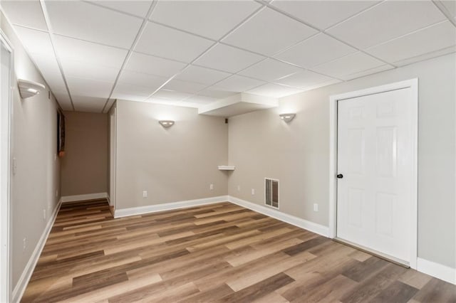 basement featuring baseboards, a drop ceiling, light wood-style flooring, and visible vents