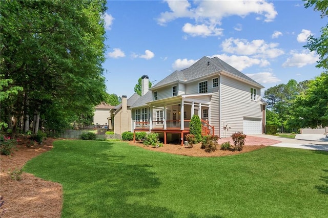 rear view of house with an attached garage, a lawn, driveway, and a chimney
