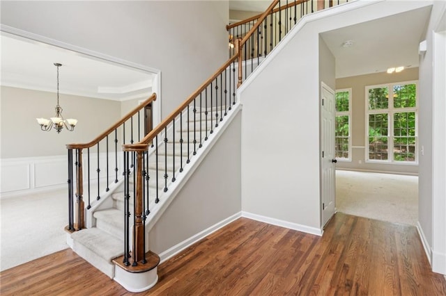 stairway featuring baseboards, ornamental molding, wood finished floors, and a notable chandelier