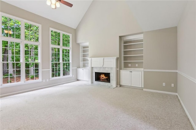 unfurnished living room featuring ceiling fan, built in features, a fireplace, baseboards, and carpet flooring