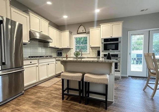 239 Lenore Ct, Hiram, GA 30141 - kitchen with appliances with stainless steel finishes, under cabinet range hood, dark wood-style flooring, backsplash, and a kitchen bar