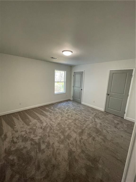 empty room with visible vents, baseboards, and dark colored carpet