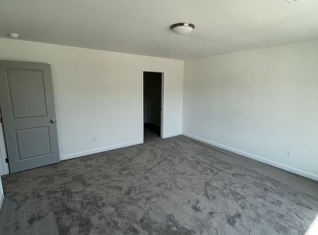 empty room featuring dark carpet and baseboards