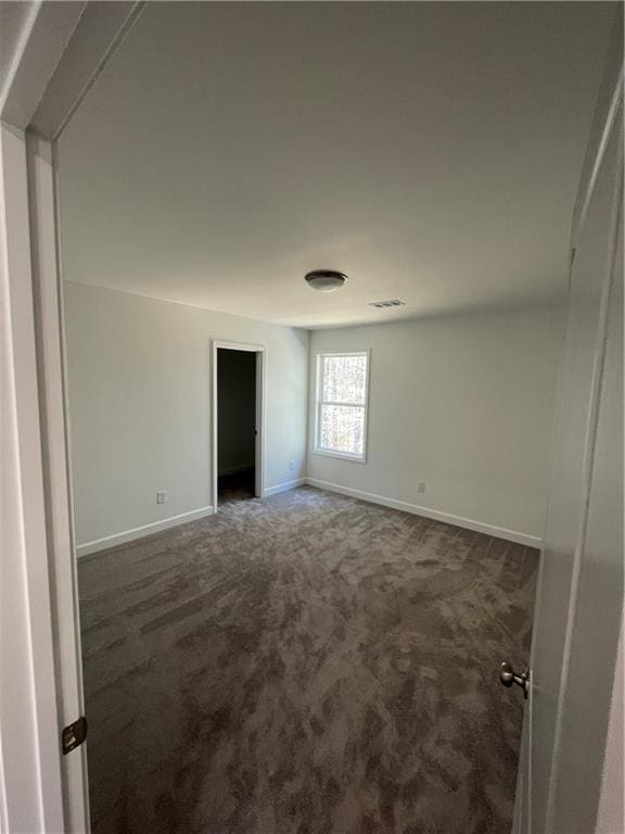 spare room with visible vents, dark carpet, and baseboards