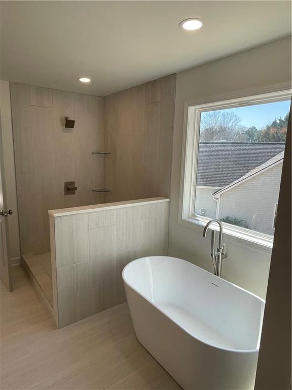 bathroom featuring recessed lighting, a freestanding bath, walk in shower, and wood finished floors