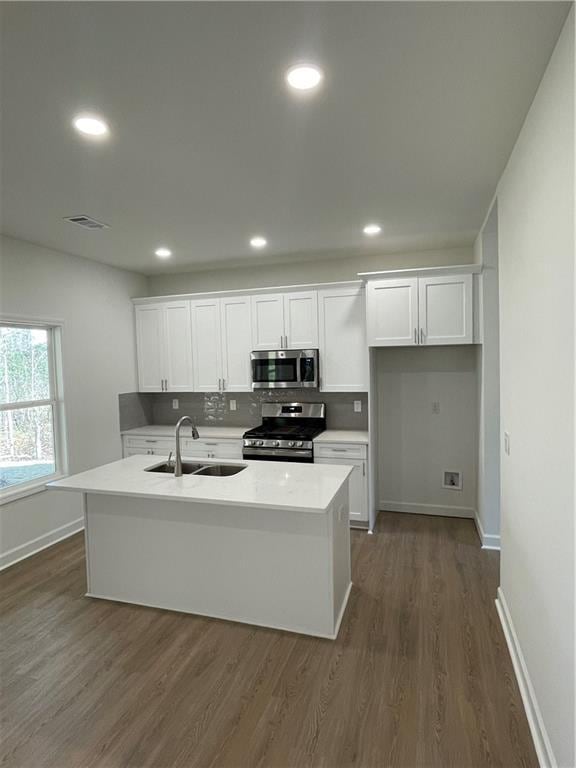 kitchen with a sink, stainless steel appliances, dark wood-type flooring, and white cabinetry