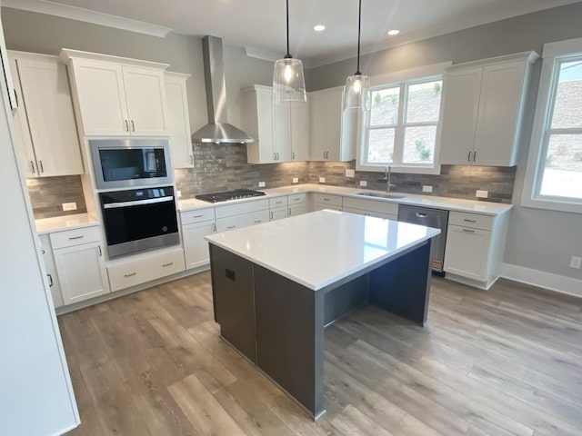 kitchen featuring a sink, light countertops, appliances with stainless steel finishes, wall chimney range hood, and light wood-type flooring