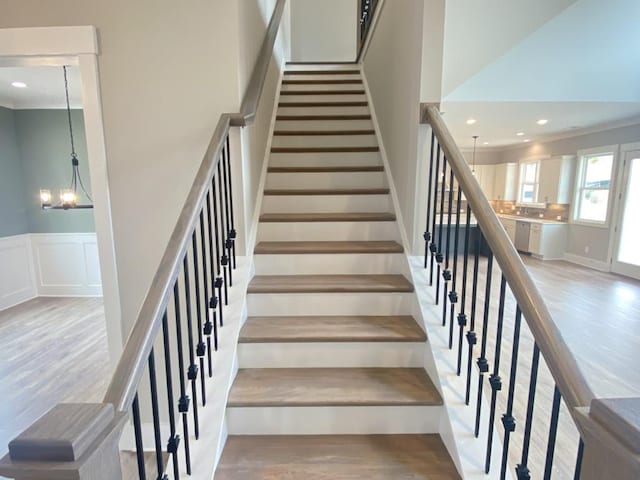 stairway with a notable chandelier, a decorative wall, wood finished floors, and wainscoting