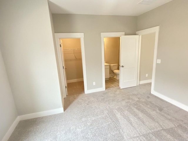 unfurnished bedroom with light carpet, baseboards, a closet, a walk in closet, and ensuite bath