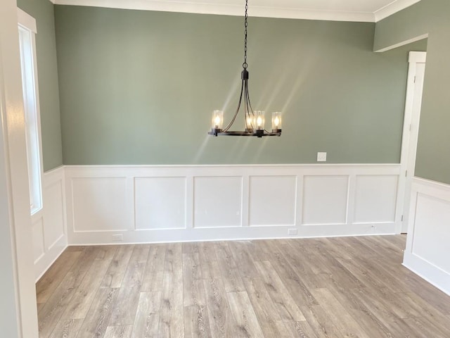 unfurnished dining area with light wood-style flooring, ornamental molding, and a notable chandelier