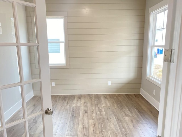 empty room with light wood finished floors, wooden walls, baseboards, and a wealth of natural light