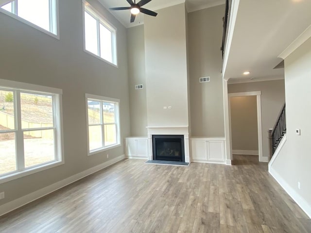 unfurnished living room with light wood finished floors, baseboards, a glass covered fireplace, stairway, and crown molding