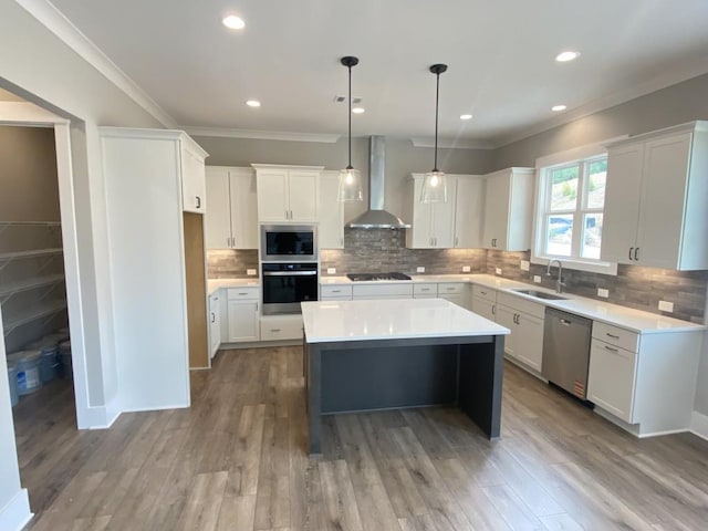 kitchen with stainless steel appliances, backsplash, a sink, a kitchen island, and wall chimney exhaust hood