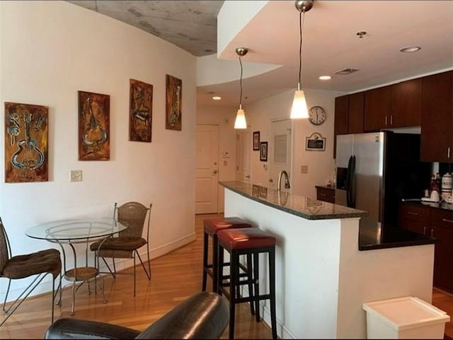 kitchen featuring an island with sink, dark brown cabinetry, stainless steel fridge, and a kitchen bar