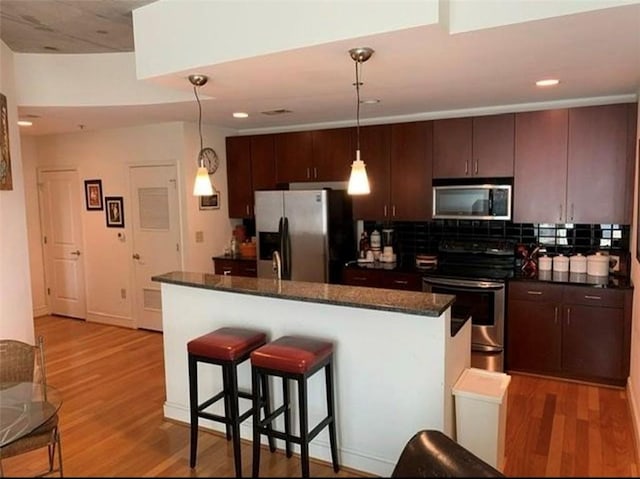 kitchen with decorative backsplash, appliances with stainless steel finishes, dark brown cabinetry, pendant lighting, and light hardwood / wood-style floors