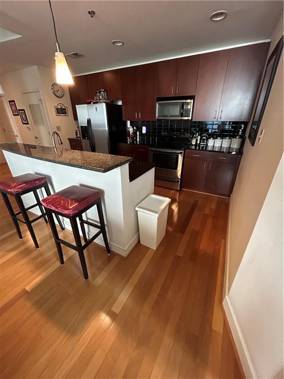 kitchen with appliances with stainless steel finishes, a breakfast bar, a center island with sink, and light hardwood / wood-style flooring