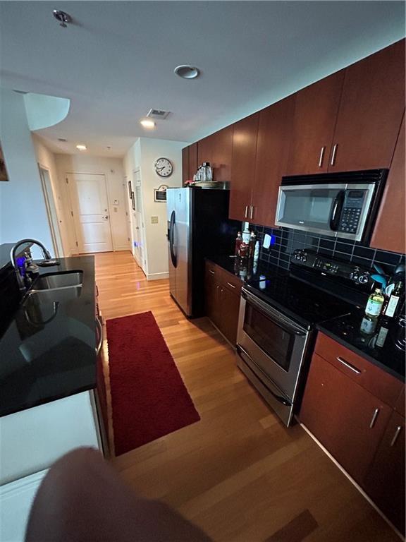 kitchen with stainless steel appliances, tasteful backsplash, sink, and light wood-type flooring