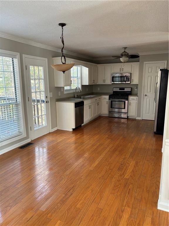 kitchen featuring stainless steel appliances, sink, white cabinets, light hardwood / wood-style floors, and hanging light fixtures