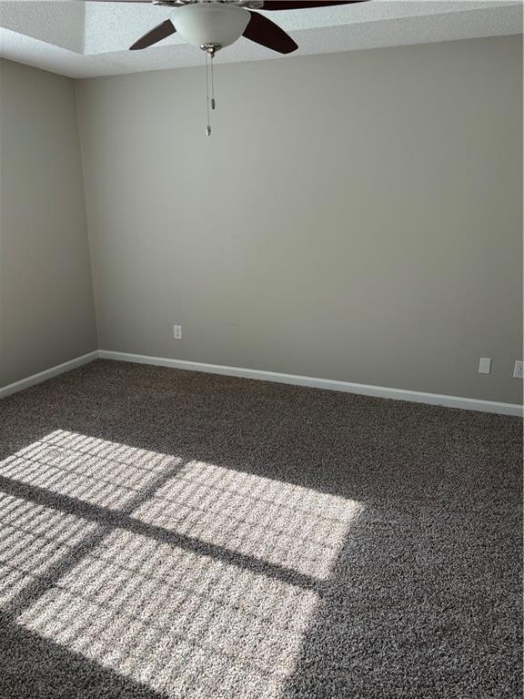 unfurnished room with ceiling fan, dark carpet, and a textured ceiling