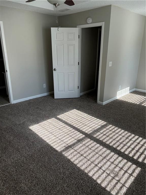 unfurnished bedroom featuring dark colored carpet, ceiling fan, and a textured ceiling