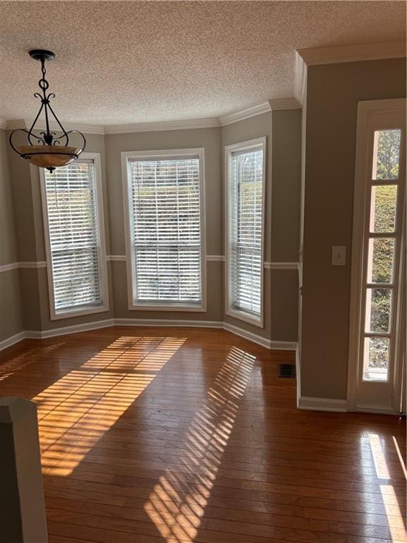 unfurnished dining area with a textured ceiling, a wealth of natural light, dark hardwood / wood-style floors, and ornamental molding