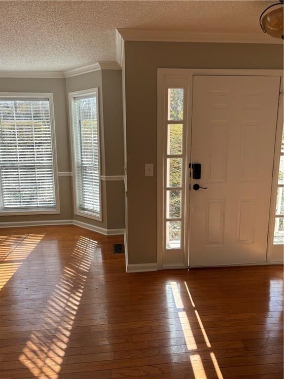 entrance foyer with crown molding, wood-type flooring, a textured ceiling, and a wealth of natural light