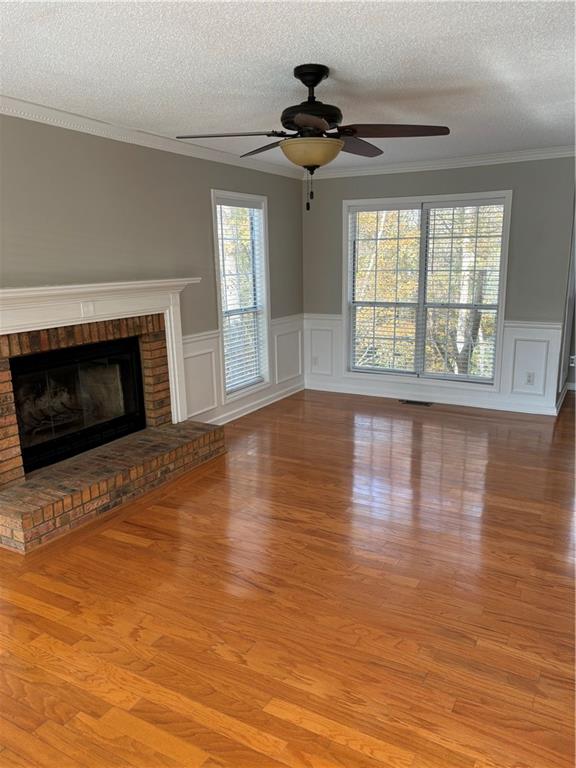 unfurnished living room featuring a wealth of natural light, a fireplace, a textured ceiling, and light wood-type flooring