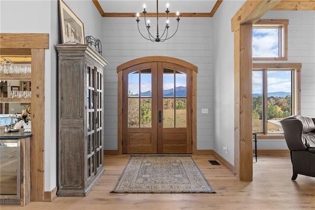 foyer with ornamental molding, light hardwood / wood-style flooring, french doors, and an inviting chandelier