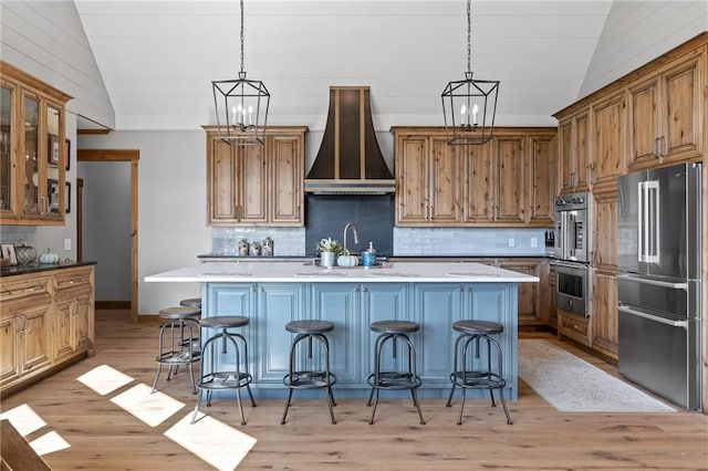 kitchen with a kitchen bar, wall chimney exhaust hood, a center island with sink, and appliances with stainless steel finishes