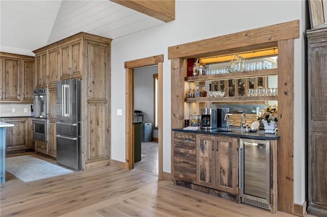 bar featuring appliances with stainless steel finishes, vaulted ceiling, light hardwood / wood-style floors, beverage cooler, and sink