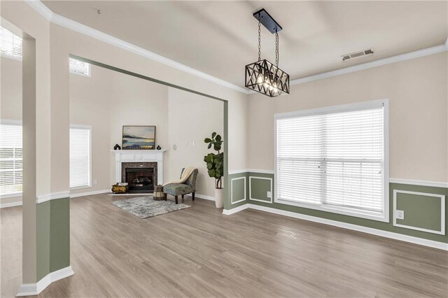 unfurnished living room with crown molding, wood finished floors, healthy amount of natural light, a chandelier, and a fireplace