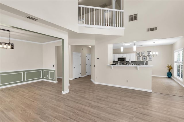 unfurnished living room with a chandelier, a high ceiling, light wood-style floors, and baseboards