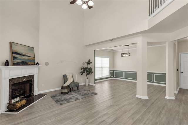 unfurnished living room featuring a high ceiling, a ceiling fan, wood finished floors, a high end fireplace, and baseboards