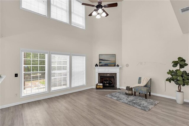 living room featuring a high ceiling, ceiling fan, wood finished floors, baseboards, and a fireplace
