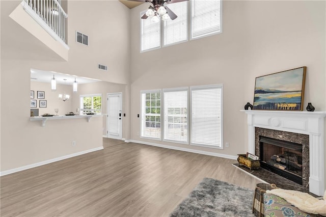 living room with a ceiling fan, a high end fireplace, wood finished floors, baseboards, and a high ceiling
