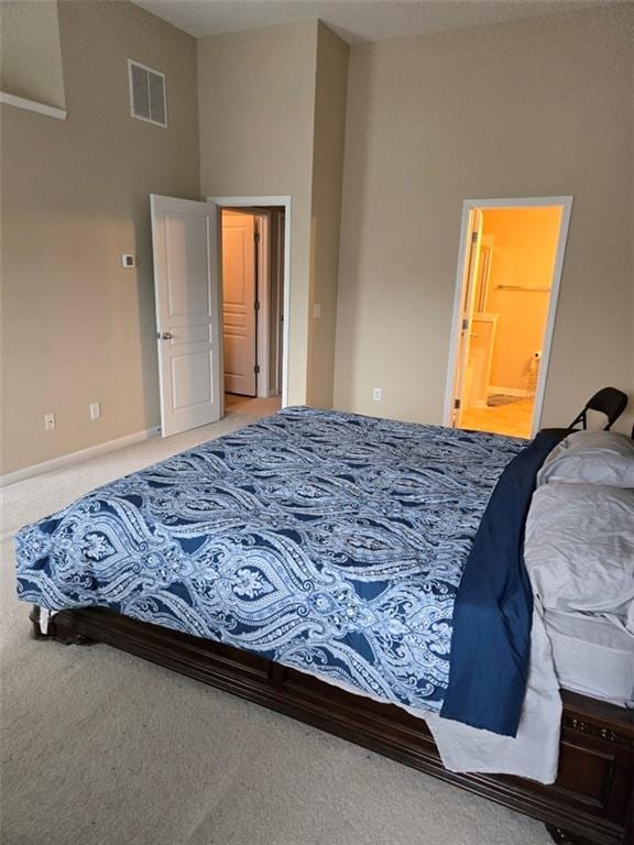 carpeted bedroom featuring ensuite bathroom, visible vents, and baseboards