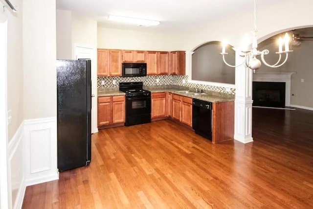 kitchen featuring a notable chandelier, backsplash, a sink, wood finished floors, and black appliances